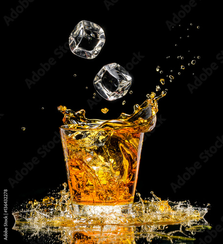 Glass of whiskey with splash on black background photo