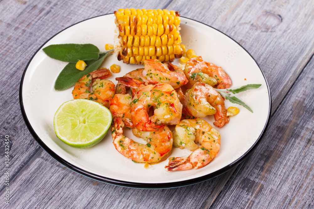 Grilled shrimps and corn garnished with lime and sage leaves. Prawns on white plate Grilled shrimps and corn garnished with lime and sage leaves. Prawns on white plate