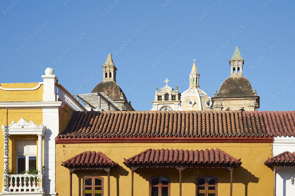 Towers and dome of the Iglesia de San Pedro Claver rise above the rooftops of historic buildings surrounding the Plaza De La Aduana in the Spanish colonial city of Cartagena de Indias, Colombia.