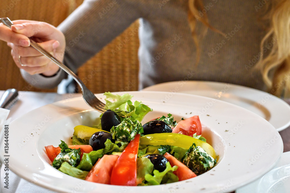 Fresh Greek salad closeup in a restaurant. Girl eating in a cafe