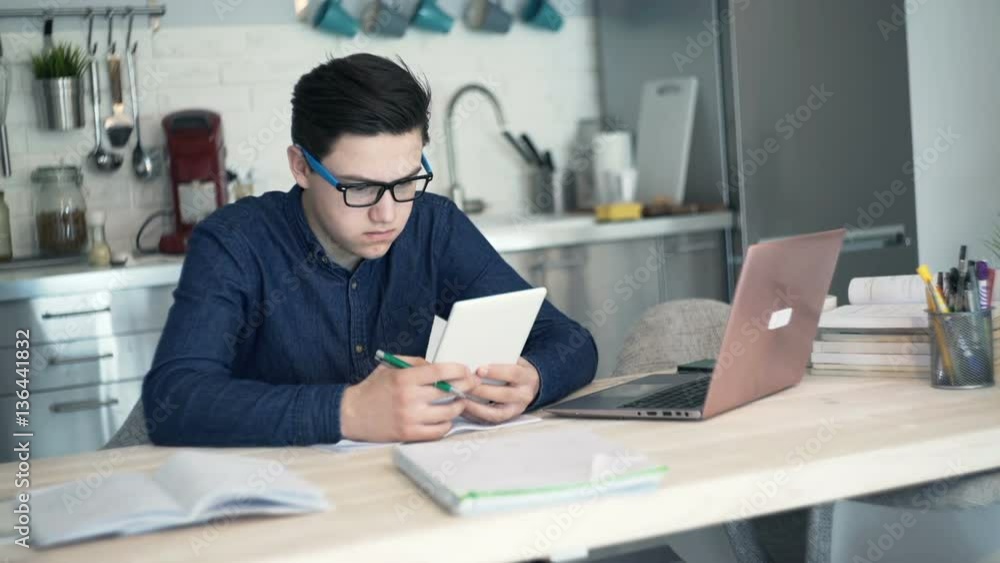 Young teenager multitasking, doing homework at home
