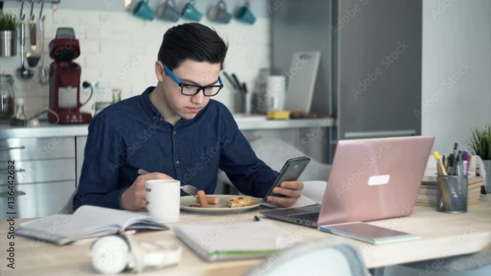 Teenager eating breakfast and texting on smartphone in kitchen at home
Teenager eating breakfast and texting on smartphone in kitchen at home