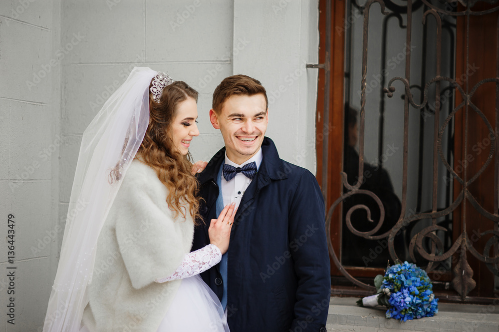 Young wedding couple at cold winter day against white stone wall