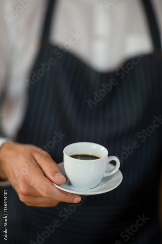 Mid-section of waiter standing with cup of coffee