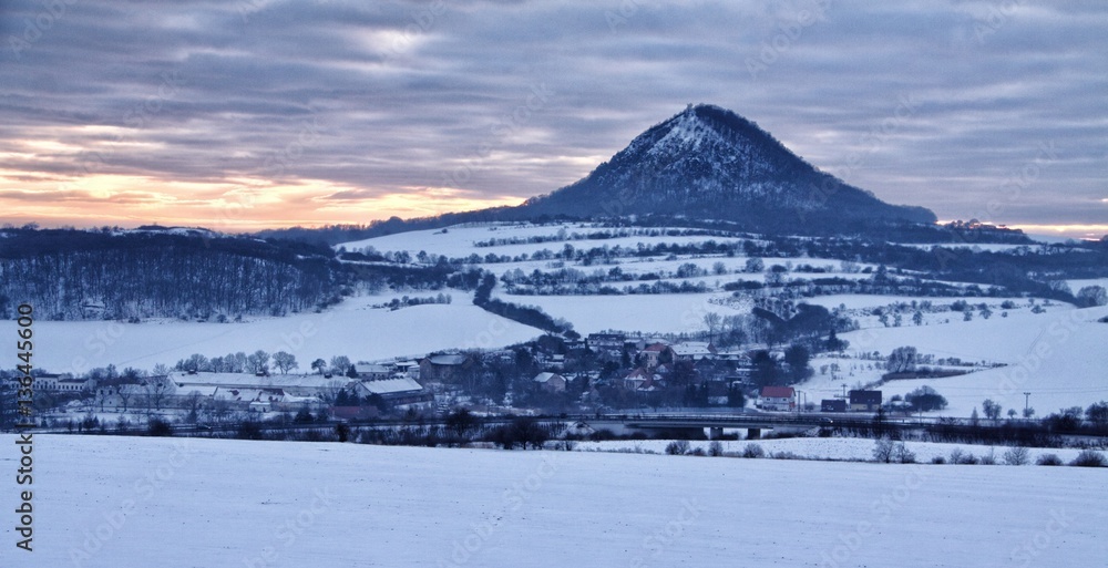 Snow covered landscape with steep hill by dusk