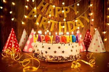 Happy birthday cake with candles on the background of garlands and letters.