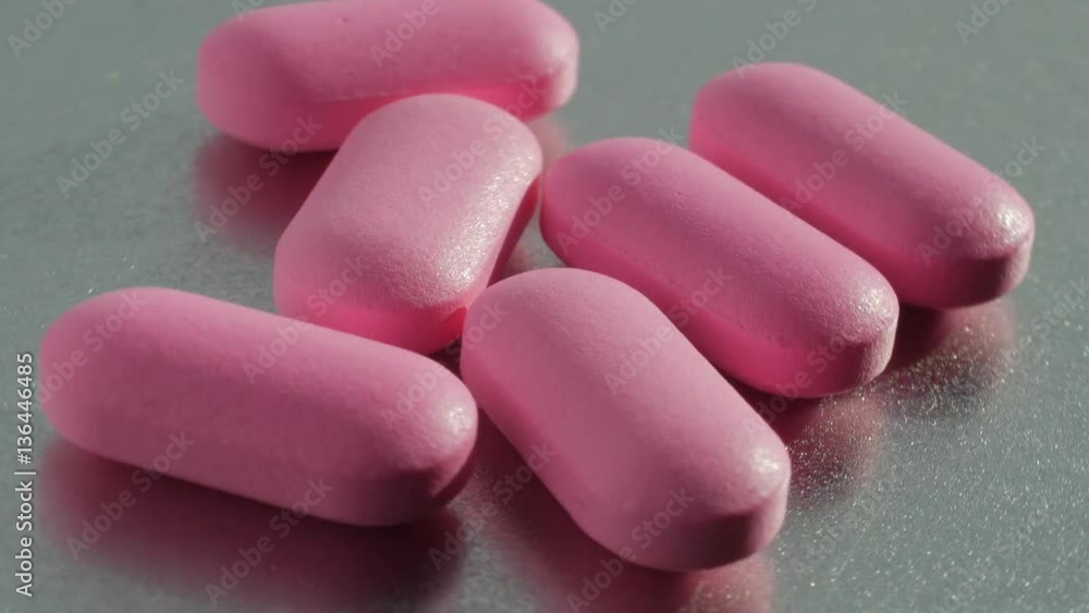 Pink medication pill turning on a table on a metal background. Pink medication pill turning on a table on a metal background.