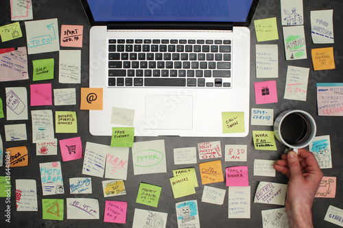 Top view on messy office desk with laptop, coffee and post it notes all around. photo