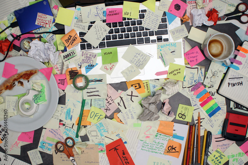 Top view on office desk with laptop computer and post it notes all around. Overwhelmed with work concept. photo