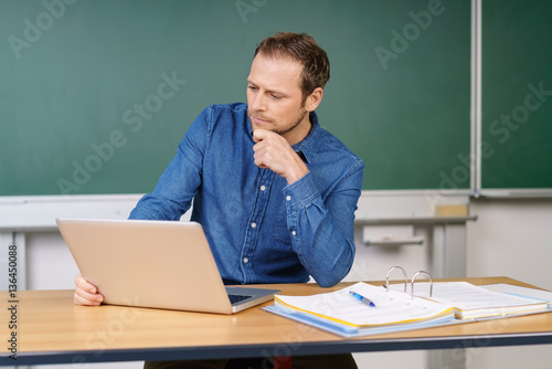 lehrer sitzt im klassenraum mit laptop und unterlagen
