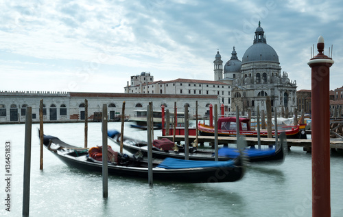 Gondolas on the Grand Canal in Venice with the Santa Mana Della Salute and blue cloudy sky in the background. © L Galbraith