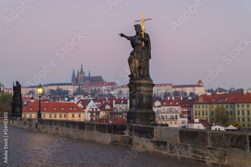 Charles Bridge at sunrise, Prague, Czech Republic. Dramatic statue and view on Prague Castle with St. Vitus Cathedral