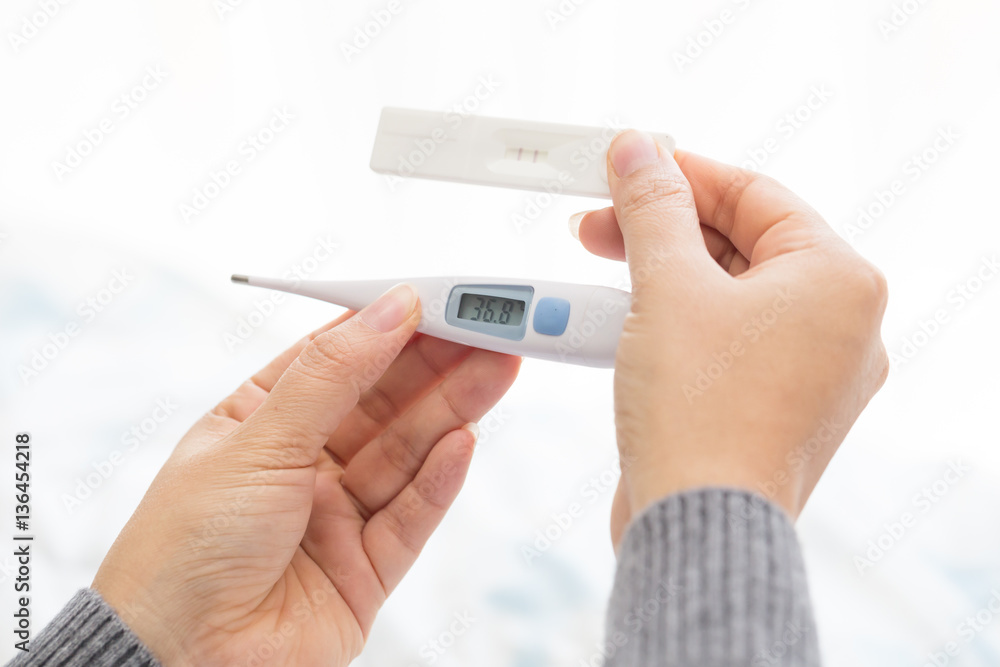 Woman hand holding thermometer and pregnant test Woman hand holding thermometer and pregnant test