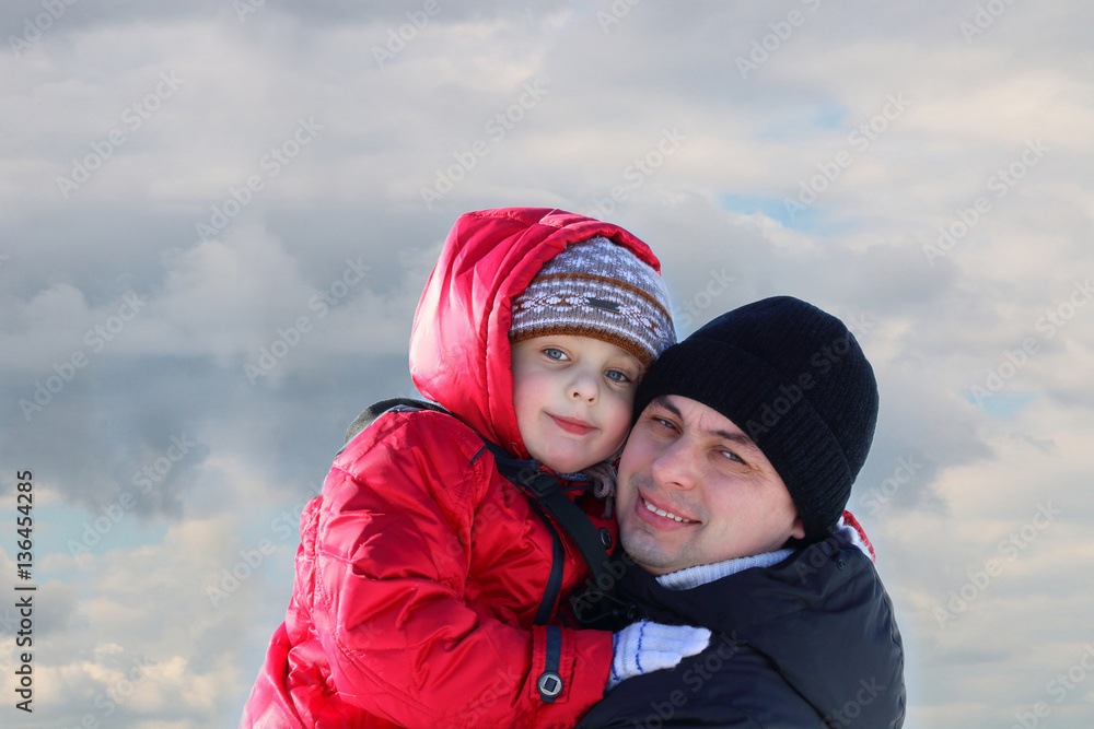 Happy family: father and little son in winter snow forest on the cloud background. Dad and boy smiling Happy family: father and little son in winter snow forest on the cloud background. Dad and boy smiling