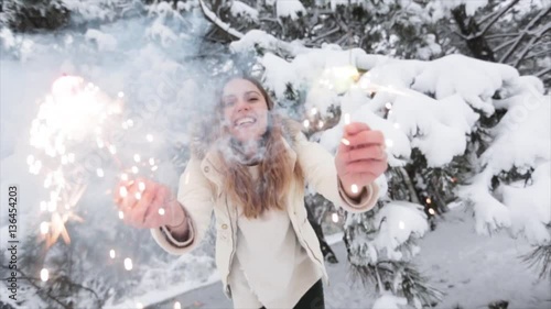 Young positive girl in winter forest snowy. Christmas and sparklers