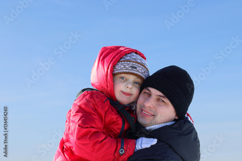 Happy father and little son in winter snow forest on the blue sky background