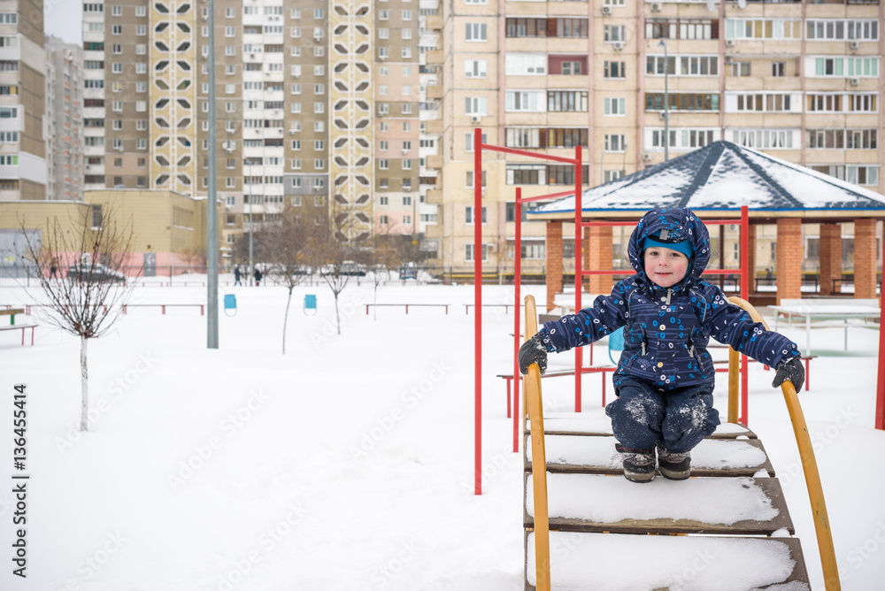 Little boy outdoors in cold winter snow. playground