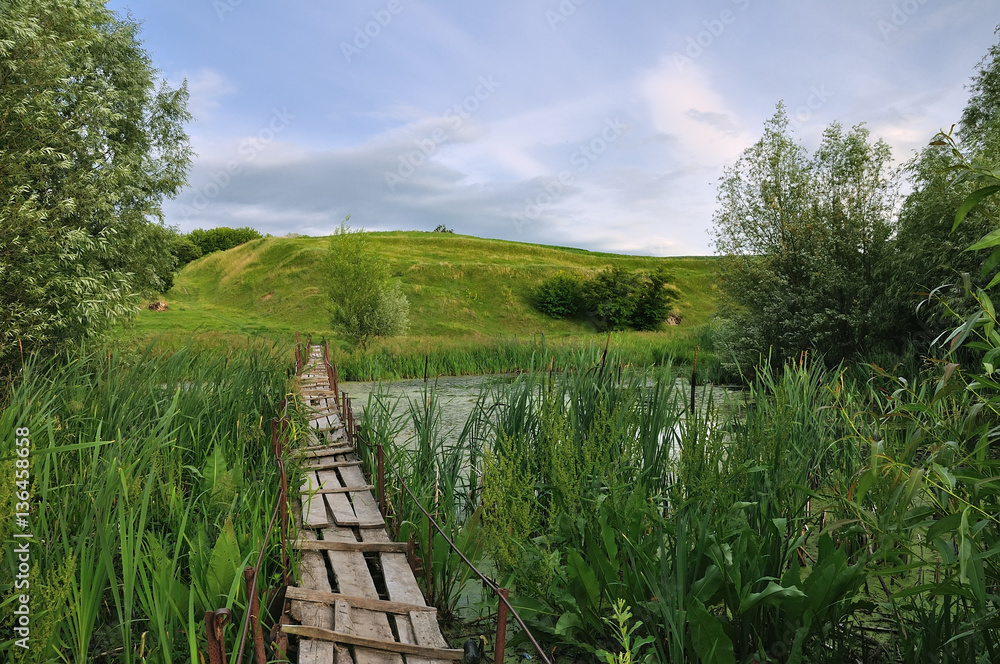A broken wooden bridge through the reeds to the green hills