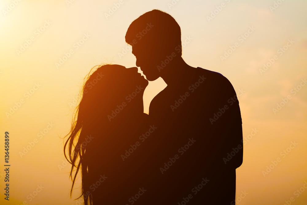 Silhouette young couple kissing over sunset background