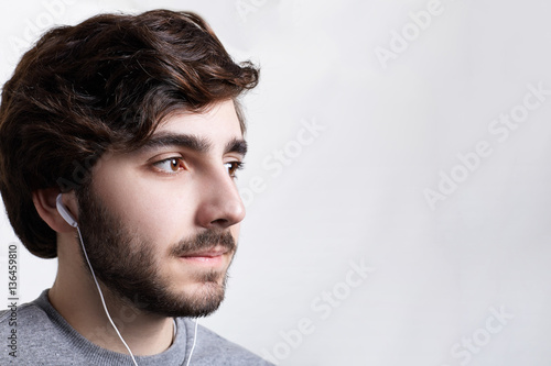 A close-up of young bearded stylish man relaxing indoors alone, listening to music tracks on earphones dreaming about something. People, leisure, fashion and technology concept.