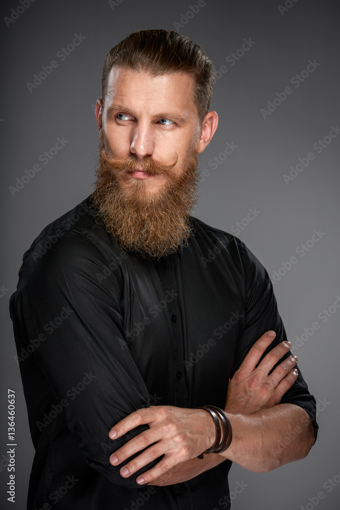Portrait of serious hipster man with beard and mustashes standing with folded hands looking back over shoulder