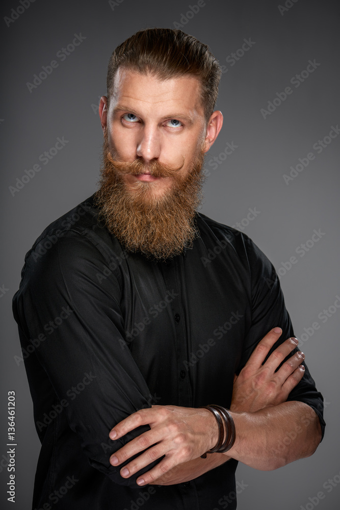 Portrait of serious hipster man with beard and mustashes standing with folded hands looking up