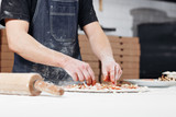 Cooking pizza. arranges meat ingredients on the dough preform. Closeup hand of chef baker in uniform blue apron cook at kitchen