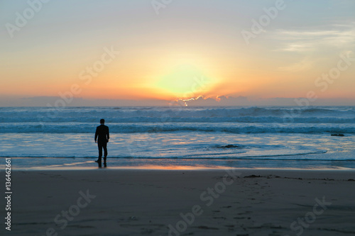 The groom in a suit on the ocean at sunset