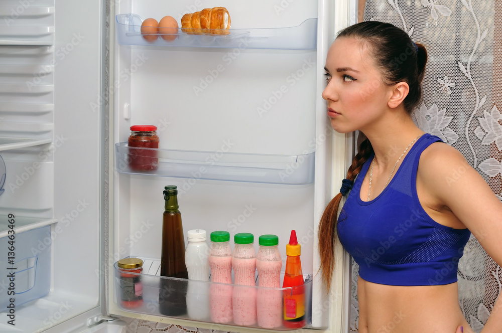 The girl looks curiously into the open refrigerator The girl looks curiously into the open refrigerator