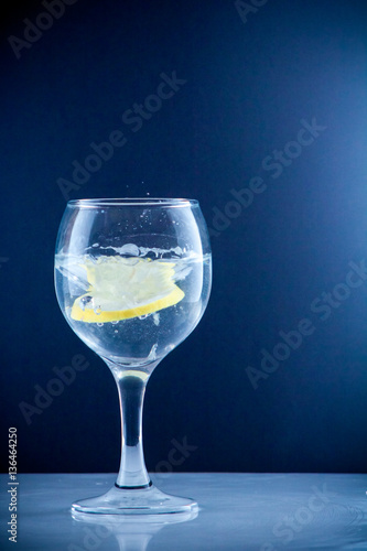 Glass glass of water with lemon on the isolated background. Mountain mineral pure mountain water with gas bubbles and a lemon slice and spray tonic refreshing sports drink.