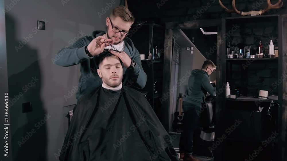 Making haircut look perfect. Young bearded man getting haircut by hairdresser while sitting in chair at barbershop, hairdresser styling. Making haircut look perfect. Young bearded man getting haircut by hairdresser while sitting in chair at barbershop, hairdresser styling.