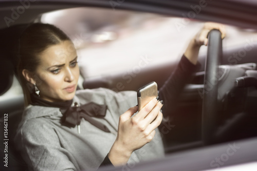 Woman texting while driving. Beautiful blonde woman driving her automobile and texting on her smartphone.