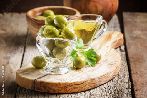 Green greek olives in glass bowl on the vintage wooden backgroun