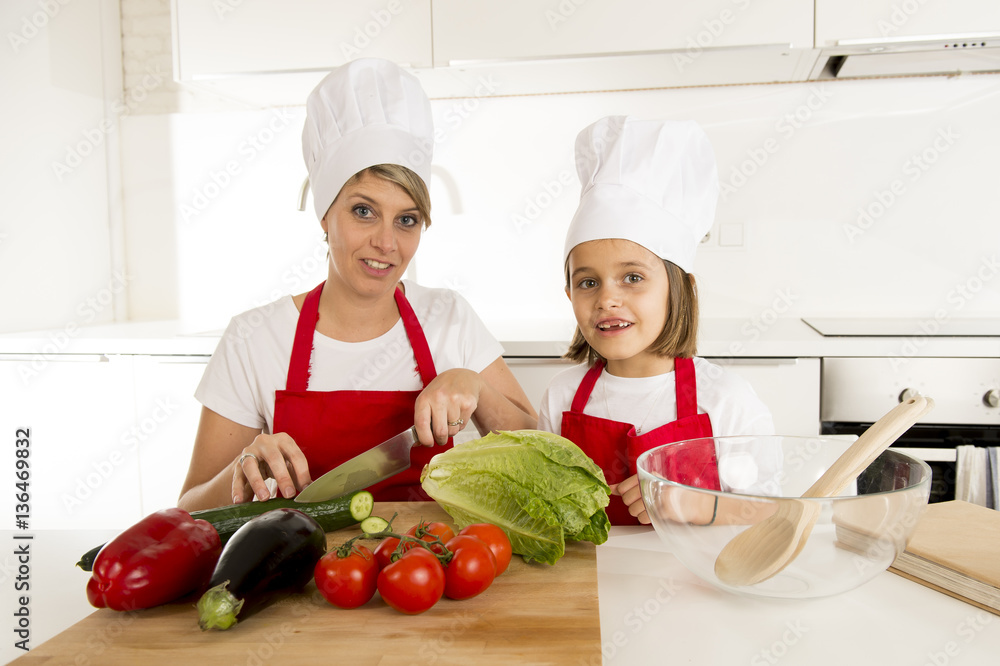 mother and little daughter cooking together with hat apron preparing salad at home kitchen mother and little daughter cooking together with hat apron preparing salad at home kitchen