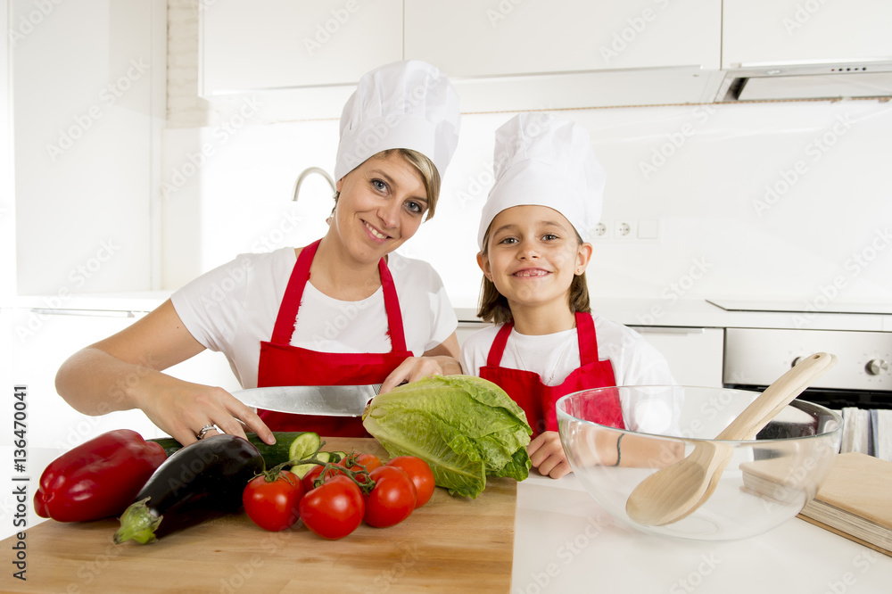 mother and little daughter cooking together with hat apron preparing salad at home kitchen mother and little daughter cooking together with hat apron preparing salad at home kitchen