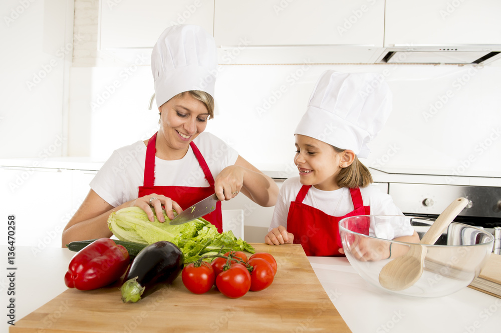 mother and little daughter cooking together with hat apron preparing salad at home kitchen mother and little daughter cooking together with hat apron preparing salad at home kitchen