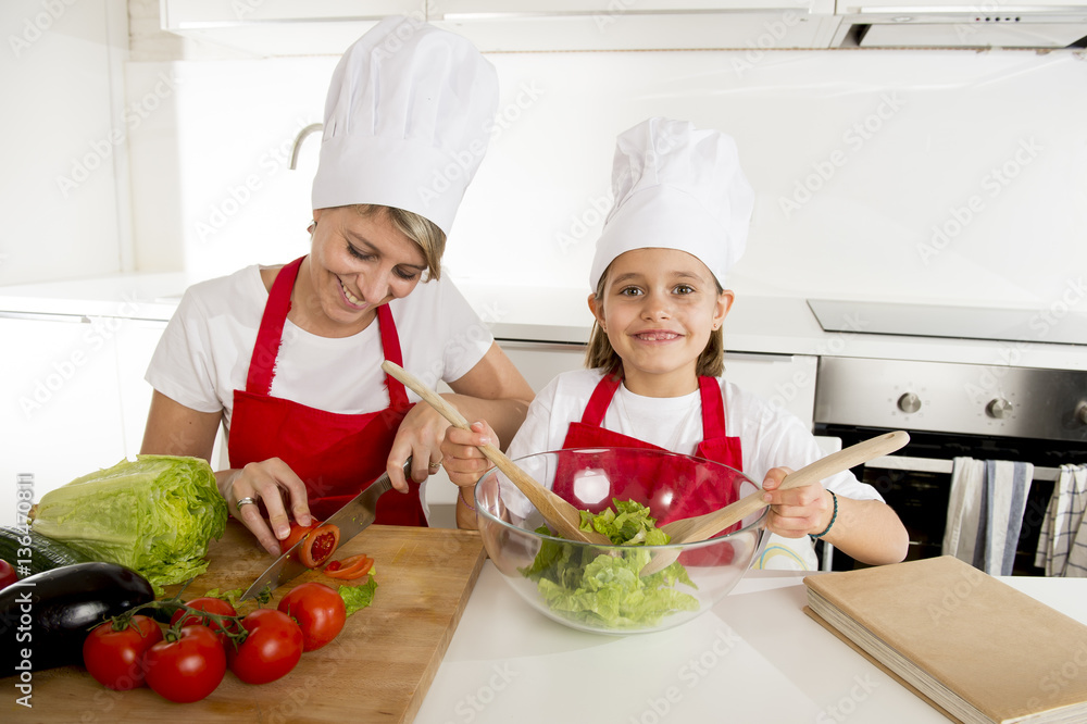 mother and little daughter cooking together with hat apron preparing salad at home kitchen mother and little daughter cooking together with hat apron preparing salad at home kitchen