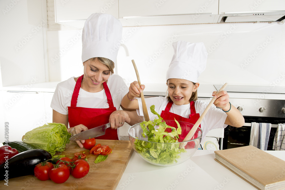 mother and little daughter cooking together with hat apron preparing salad at home kitchen mother and little daughter cooking together with hat apron preparing salad at home kitchen