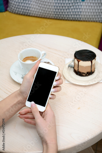 Young female using her cell phone in cafe, with cake and coffee on the side