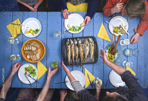 Top view on people eating grilled fish with vegetable salad and drinking vine.