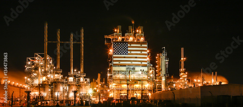 American flag on illuminated oil refinery against sky at night