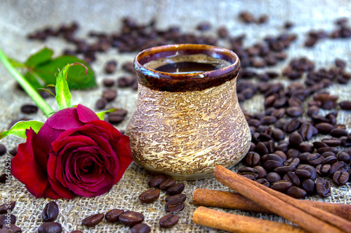 cup of black coffee with coffee beans and cinnamon, red rose on sacking