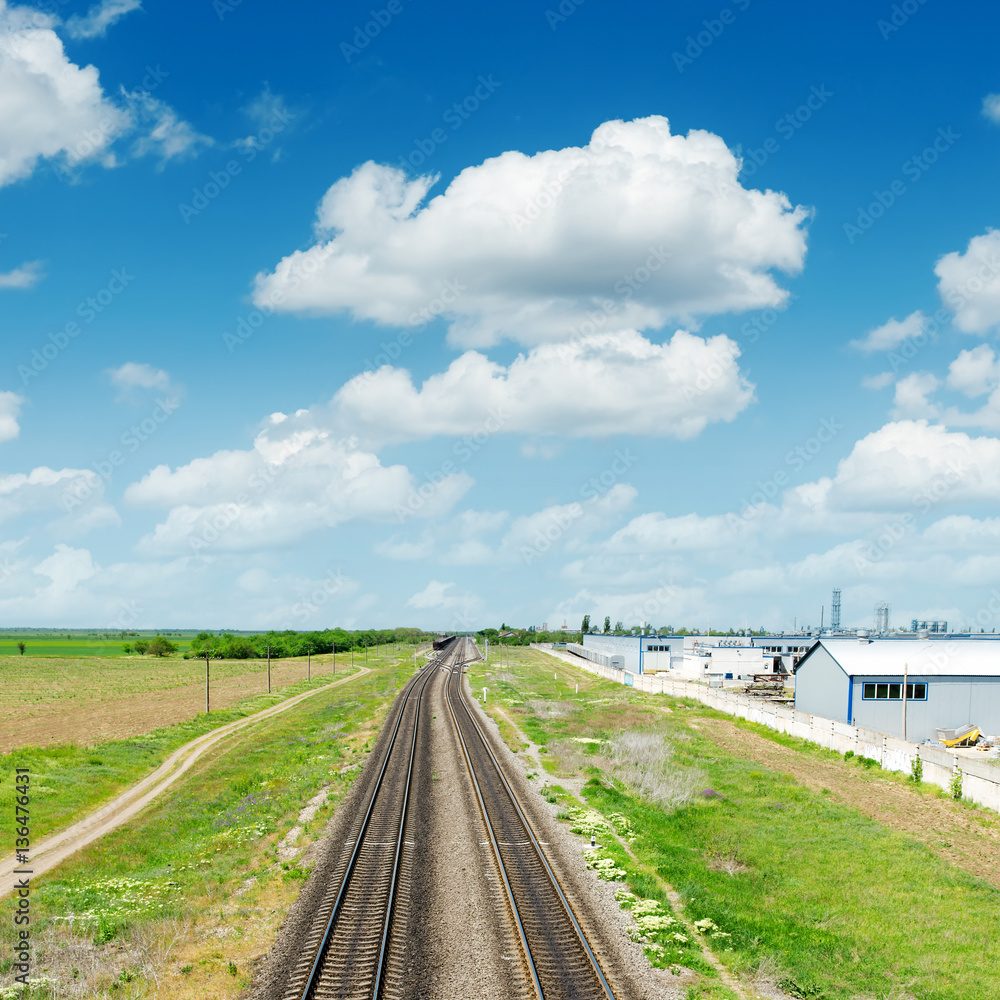 two railroads in green landscape under blue sky with clouds