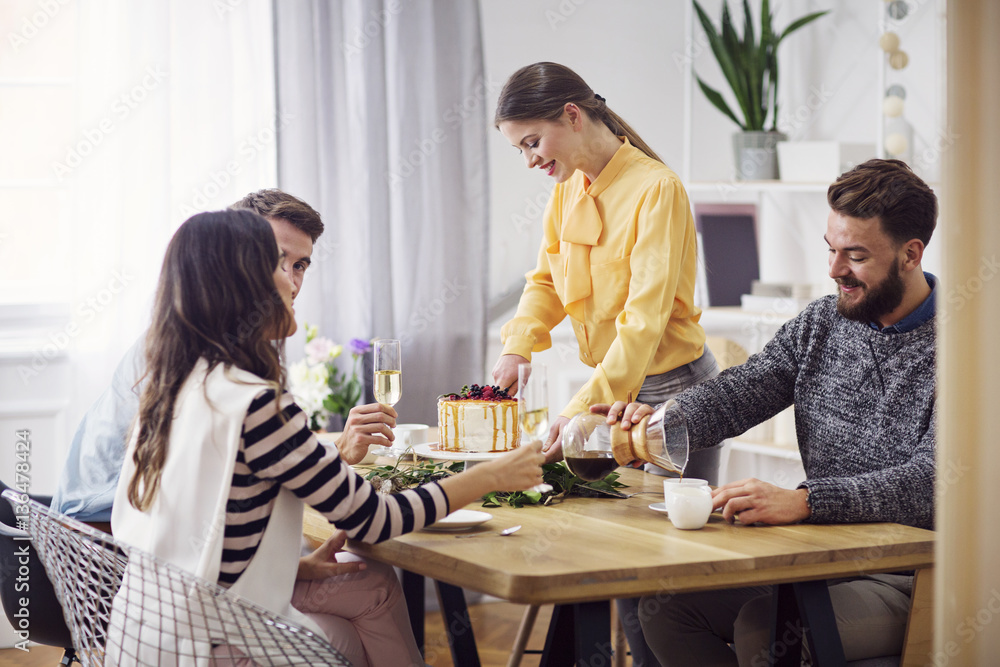 Smiling woman cutting cake while friends sitting at dinning table in party Smiling woman cutting cake while friends sitting at dinning table in party