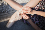 girl holding ballerina legs in pointes in a pink dress, falls the sun on the curb with stones close-up