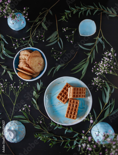 three delicious waffles, gingerbread cookies are the blue plates with herbs and flowers on a black background closeup food photo