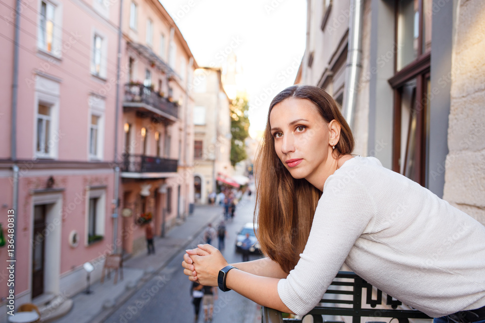 Young beautiful woman standing on the balcony and looking out on street of european city