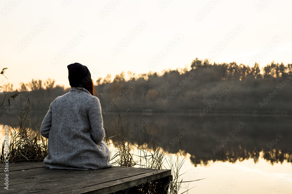 Naklejka premium mist over the lake. reeds and the girl sitting on a wooden jetty