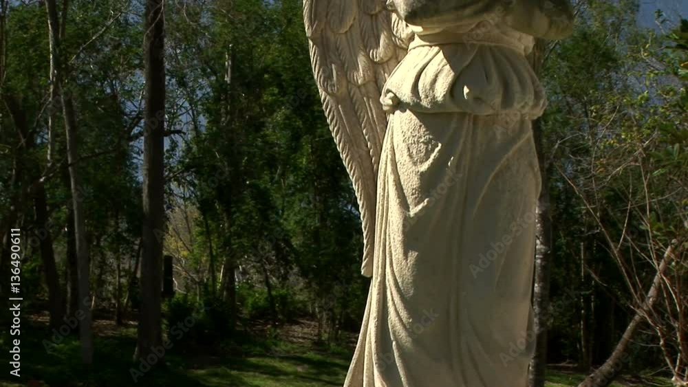 Camera moves to reveal a winged celestial image captured in stone adorning a gravesite. Camera moves to reveal a winged celestial image captured in stone adorning a gravesite.