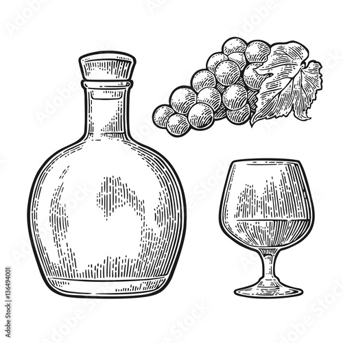 Glass and bottle of cognac with bunch of grapes.